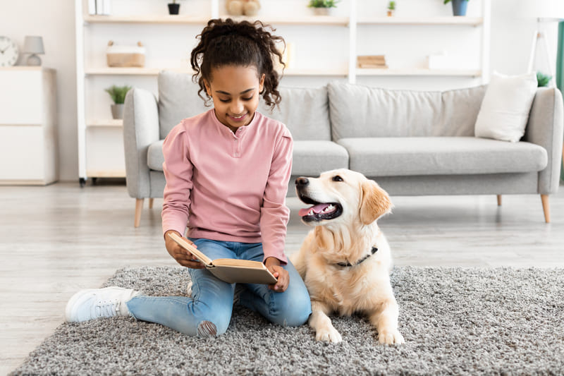 young-black-girl-reading-book-with-dog-at-home